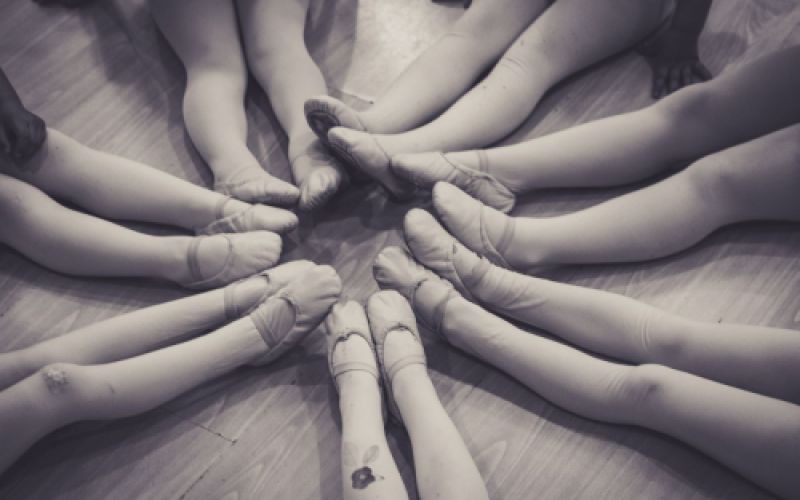 Imagen en blanco y negro de piernas de niñas con zapatillas de ballet sentadas en círculo