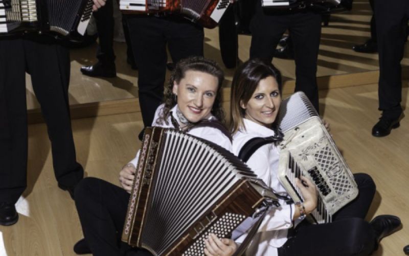 Imagen de grupo de personas y dos chicas sentadas totas ellas con un acordeón